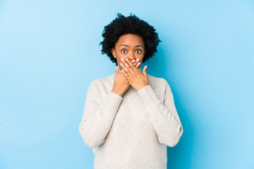 Middle aged african american woman against a blue background isolated shocked covering mouth with...
