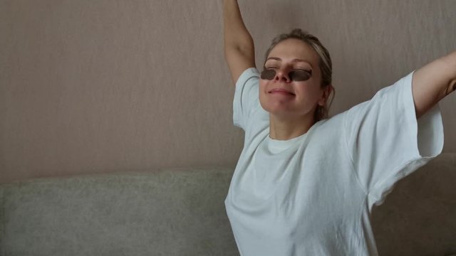 a young beautiful girl with black eye patches did not get enough sleep. a woman in a white t-shirt on the bed