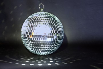 Mirror ball against a black background.  The mirror ball is reflecting a geometric pattern on the dark foreground. Light is reflected off the mirror ball.