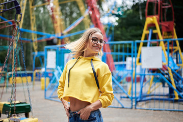Young blond woman, wearing yellow hoody, blue jeans, spending time in amusement theme park in...