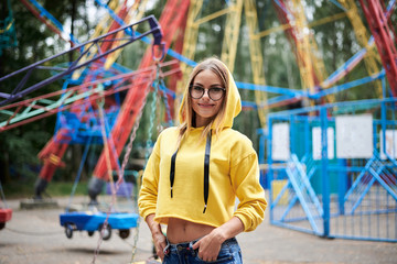 Young blond woman, wearing yellow hoody and blue jeans, spending time in amusement theme park in...