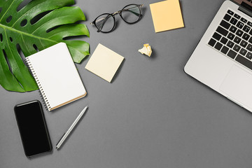 Workspace with modern smartphone, laptop, pen, monstera leaves, eyeglasses and notebook on grey background minimal style. Flat lay, top view office table desk. Template for blog social media
