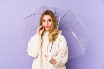 Young blonde woman holding an umbrella isolated Young blonde woman holding an umbrella isolated with fingers on lips keeping a secret.