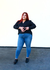 Happy smiling red-haired overweight woman is standing on stone floor. Young plus size female model...