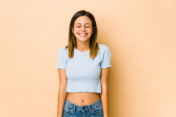 Young woman isolated on beige background laughs and closes eyes, feels relaxed and happy.