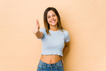 Young woman isolated on beige background smiling and raising thumb up