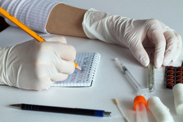 female doctor writing a prescription. A doctor in white gloves writes a prescription for treatment on a white table with medicines, bandages, syringes and a thermometer.