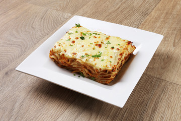 classic lasagna bolognese Portion isolated served on a white plate on wooden table background