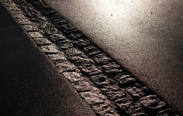 shiny wet asphalt road with cobblestone gutter