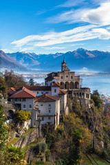 Fototapeta na wymiar Stunning panorama view of Madonna del Sasso church above Locarno city on cliff with Lake Maggiore, snow covered Swiss Alps mountain peaks blue sky cloud in background in autumn, Ticino, Switzerland