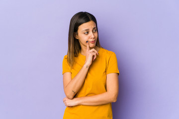 Young woman isolated on purple background looking sideways with doubtful and skeptical expression.