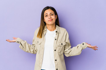 Young woman isolated on purple background doubting and shrugging shoulders in questioning gesture.