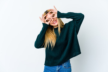 Young blonde woman isolated on white background showing okay sign over eyes