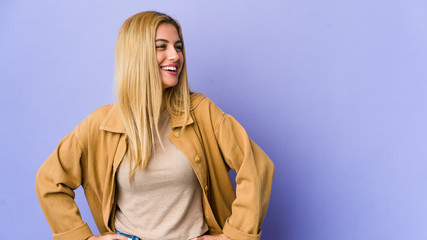 Young blonde woman isolated on purple background confident keeping hands on hips.