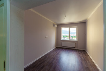 An empty room with white walls and wooden floors . Fresh new renovation. The door to the corridor.