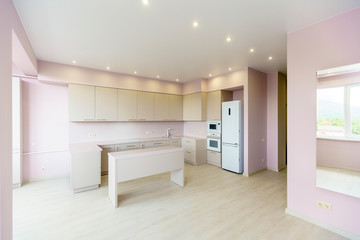 New kitchen furniture  set in white colors in the style of minimalism in a new building. pink wall. kitchen appliances: refrigerator, gas stove with oven. Table in front of the kitchen