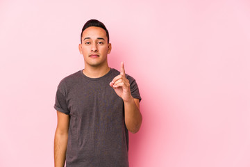 Yooung latin man posing in a pink backgroundshowing number one with finger.