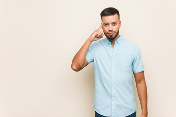 Young south-asian man pointing temple with finger, thinking, focused on a task.