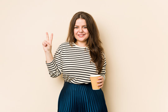 Young curvy woman holding a coffee showing number two with fingers.