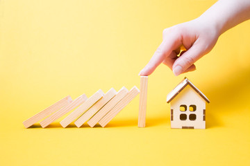 hand stops falling wooden dominoes Falling On House Model, real estate protection concept, yellow...