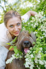 Naklejka premium A young girl in a white dress is in the park with her pet dog briard.Spring time.