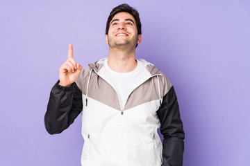 Young man isolated on purple background indicates with both fore fingers up showing a blank space.