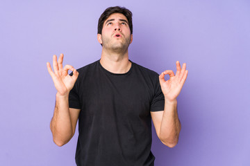 Fototapeta premium Young man isolated on purple background relaxes after hard working day, she is performing yoga.