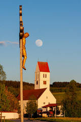 Feldkreuz mit Mond und Kirche von Haisterkirch in Oberschwaben im Hintergrund