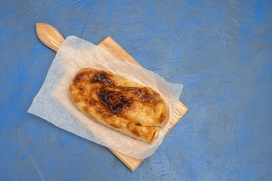 Top view of Bulgarian traditional cheese pie Banitsa (Banica, Banitza) on wooden board on dark blue background with copy space
