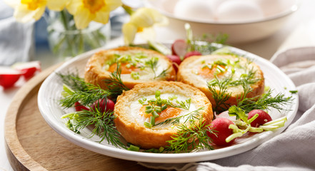 Delicious breakfast baked eggs in bread bowls with the addition of fresh herbs and radishes on a white plate