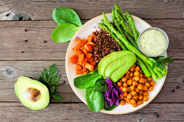 Healthy Buddha bowl with asparagus, quinoa, sweet potato, chickpeas and avocado. Above view over a rustic wood background.