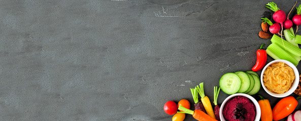 Assortment of fresh vegetables and hummus. Above view corner border on a dark slate banner...