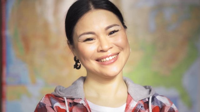 Teacher or student with USA geography map on background. Pretty brunette asian woman standing in plaid shirt and smiling with arms crossed. Happy asian immigrant posing on USA map background.