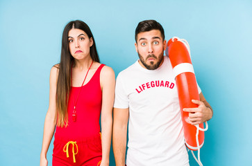 Young lifeguard couple isolated shrugs shoulders and open eyes confused.