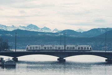Tram in Zurich on bridge over lake. Mountain skyline