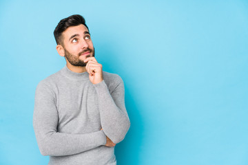 Young caucasian man against a blue background isolated looking sideways with doubtful and skeptical...