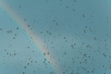 A rainbow behind a glass windows with water drops.