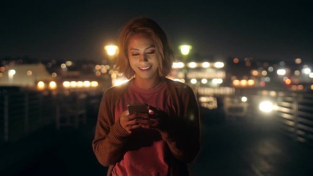 Portrait of happy casual young millenial woman chatting use smartphone on balcony at night