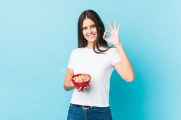 Young caucasian woman holding a cereals bowl cheerful and confident showing ok gesture.