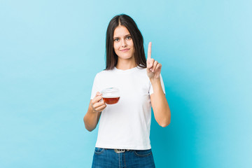 Young caucasian woman holding a tea cup showing number one with finger.