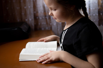 little girl reading a book at home, the child learns at home, girl with pigtail