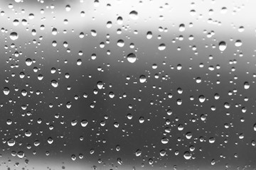 Water droplets from a rain shower on glass with a gray silver background.