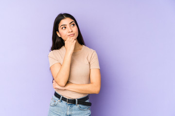 Young indian woman isolated on purple background relaxed thinking about something looking at a copy...