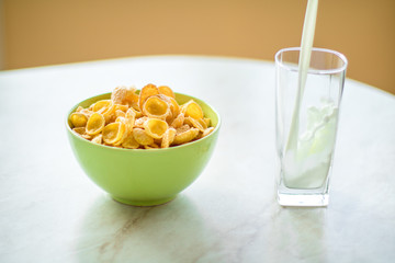 cornflakes in the green dish, milk is flowing into the glass
