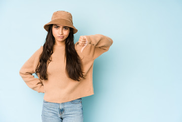 Young indian woman wearing a hat isolated on blue background showing thumb down, disappointment concept.