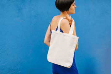Woman holding canvas tote bag on bright blue background in the city. Reusable eco bag. Eco friendly concept.