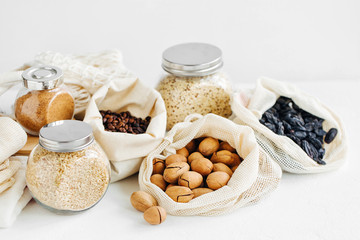 Nuts, dried fruits and  groats  in eco cotton bags and glass jars on white table in the kitchen. Zero Waste Food Shopping.  Waste-free living