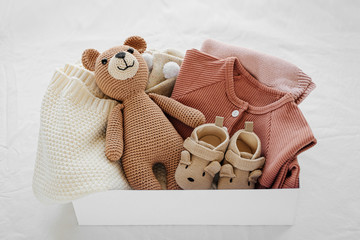 Box with baby stuff and accessories for newborn on bed. Gift box with knitted blanket, clothes,...