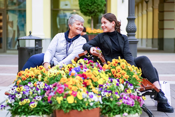A young girl is talking to an elderly woman sitting on a bench among flowers.