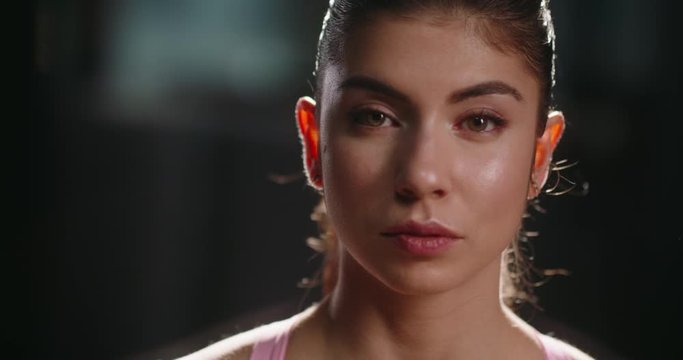 Close-up portrait of beautiful motivated female athlete looking at camera. Young bodybuilding girl during training workout session - sports concept 4k footage